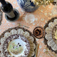 Pomegranate Clay hand block printed cotton tablecloth set with silver forks, a scalloped wicker charger and a brown transferware plate